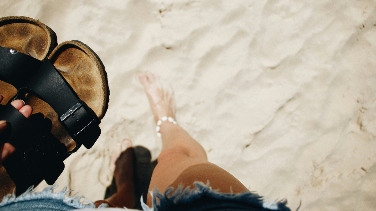 une paire de sandale tenue dans les mains d'une femme a la plage